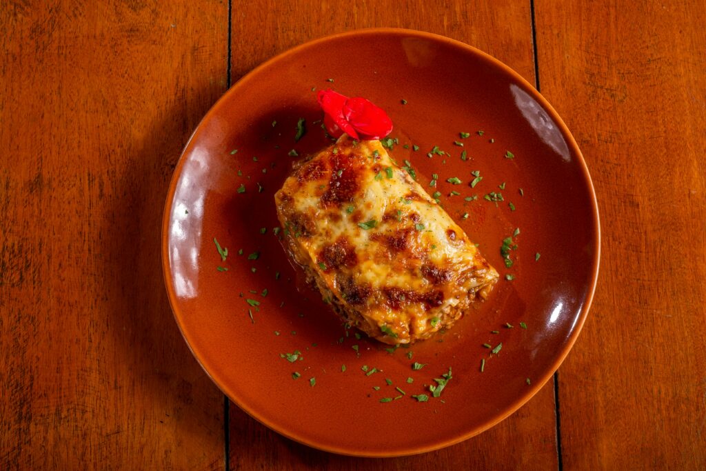 Top-down view of mouth-watering lasagna served on an orange plate with garnish.