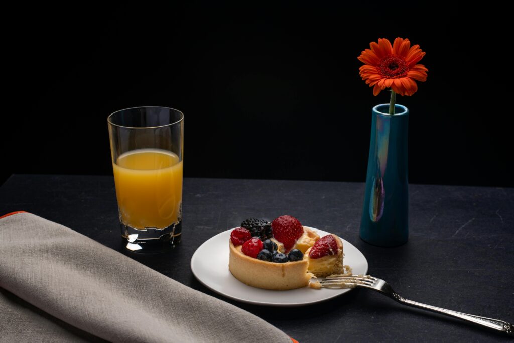 High angle of plate with delicious cheesecake decorated with berries placed on table with orange juice and vase with red gerbera