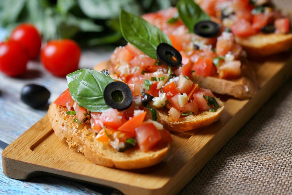 Close-up of delicious bruschetta topped with tomatoes, olives, and basil on a wooden board.